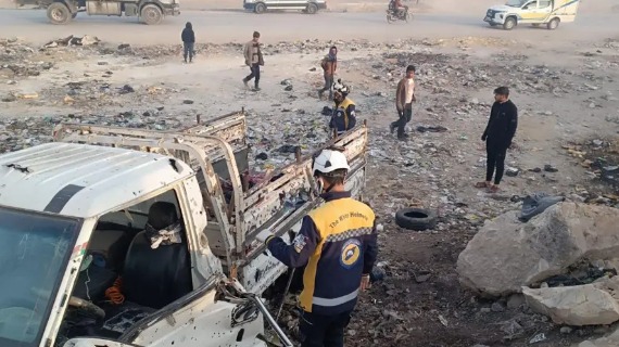 A first respondent wearing a White Helmet surveys the remains of a vehicle