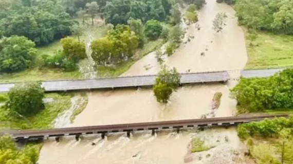 An aerial view shows two roads over an overflowing muddy river, one of them is partially collapsed