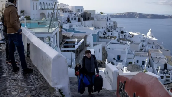 A man carries a suitcase up steep stairs in the old port of Fira on the island of Sanrtorini