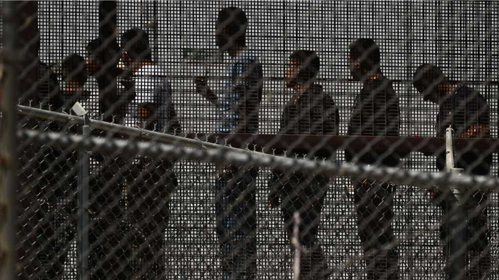 Migrants silhouettec behind a wire fence