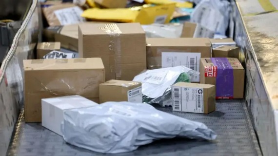 Small cardboard parcels and white plastic envelopes are transported on a conveyor belt.