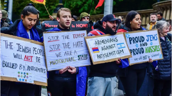 Demonstrators at a rally against antisemitism hold up signs reading ' The Jewish people will not be bullied by antisemites', 'stop the terror, stop the hate, we are a multicultural state', 'Armenians against antisemitism' and 'proud Jews and proud Aussies'