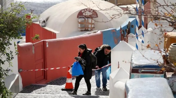 Two people walk past a tape closing off a street in Santorini