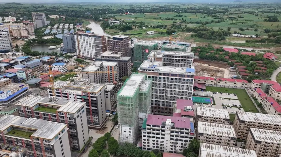 An aeria view of Shwe Kokko shows several high-rises, some of them under construction. The Moei river and cornfields can be seen in the distance.