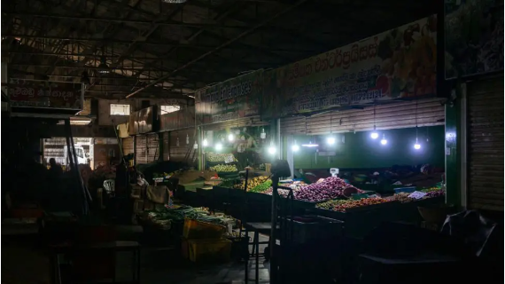 A few lamps illuminate produce an otherwise pitch-black market 