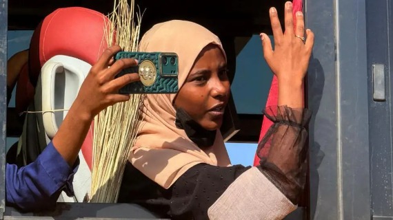 A woman wearing a hijab holds up a hand while another takes a picture with her phone