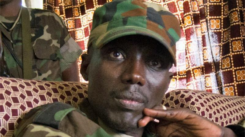 A head shot of Sultani Makenga. He wears a military-style cap and a camouflage jacket