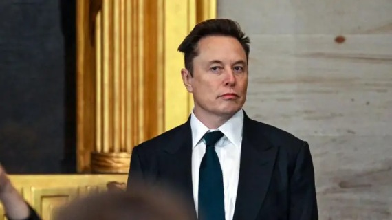 Elon Musk wears a black suit, a white shirt and a dark green tie.