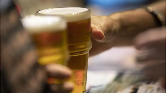 A hand reaches to grab one of two glasses filled with beer standing at a bar.