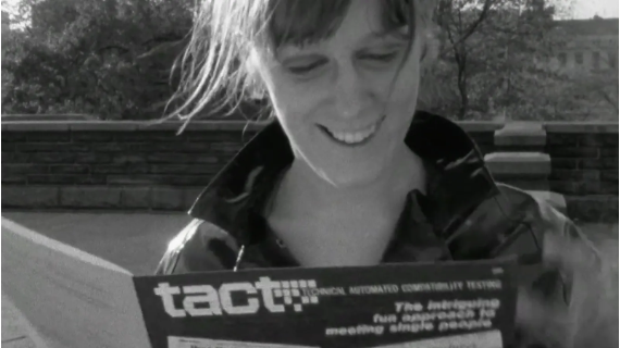 A black and white screenshot shows a woman smiling while reading a leaflet titled Tact